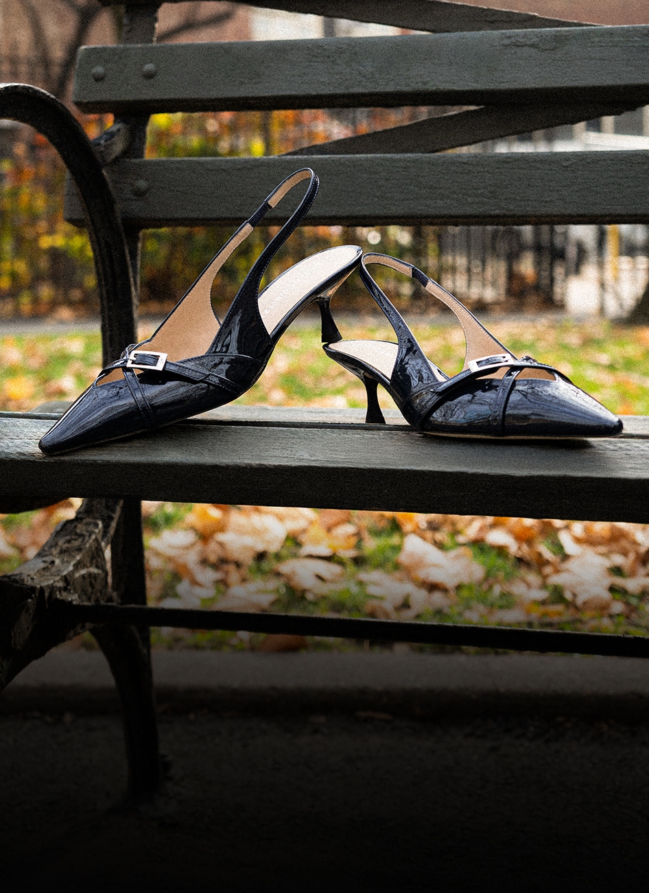 Black leather slingback heels with buckle displayed on a park bench.